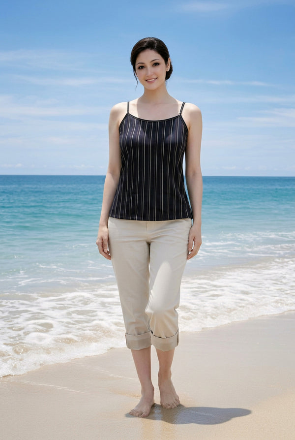 A woman modeling a black ribbed camisole tank top and beige rolled capri pants against a solid dark gray background.