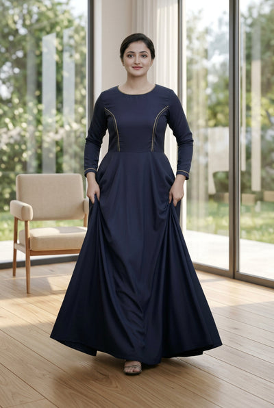Woman in a long dark blue dress standing outdoors with greenery in the background